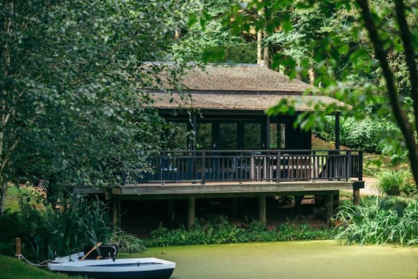 An Image of the lakehouse with a lake under the stilts of the house and framed by the leaves of trees either side.